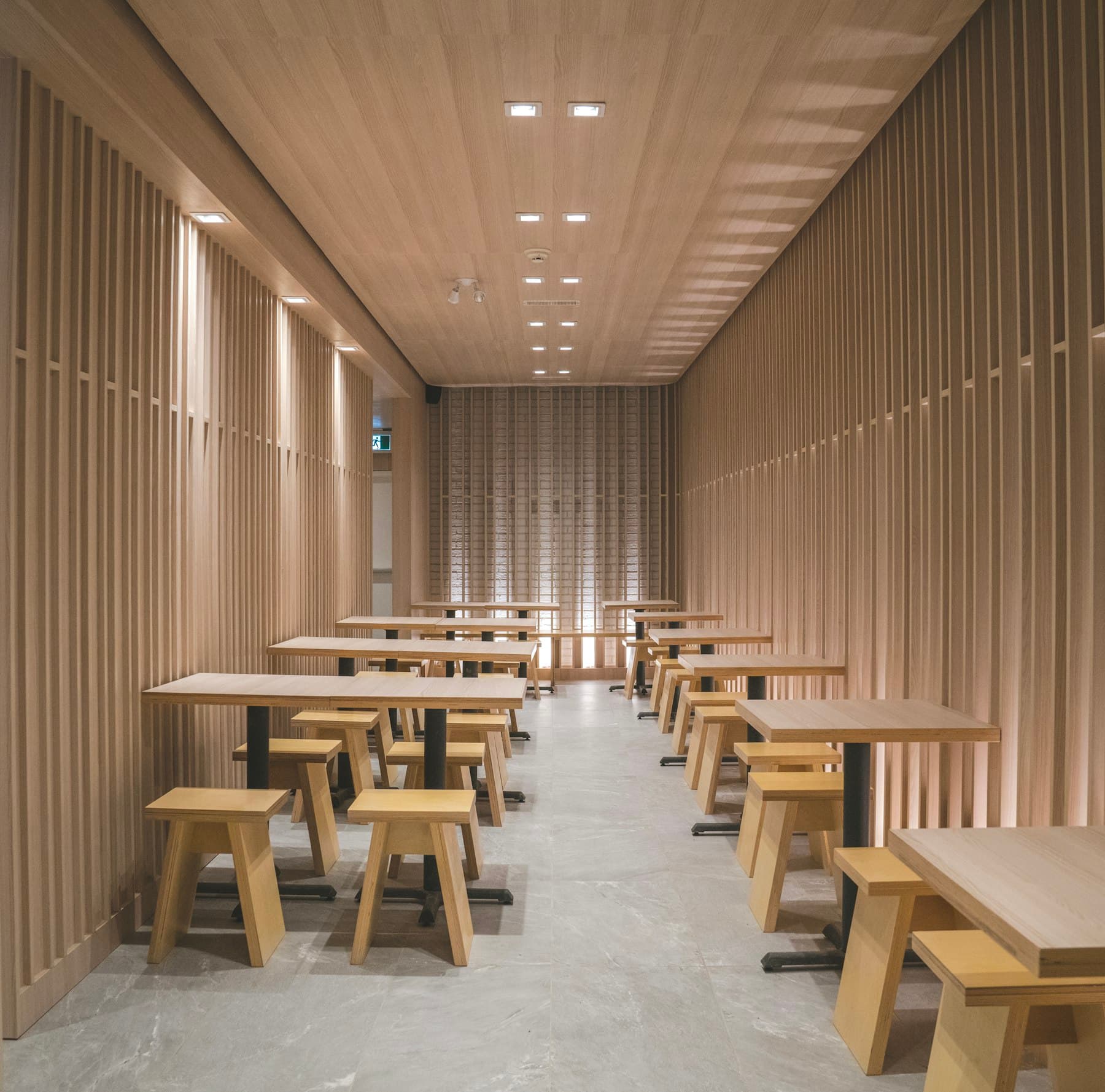 Sala alargada de un café forrada de lamas de madera clara, con mesas y taburetes a ambos lados