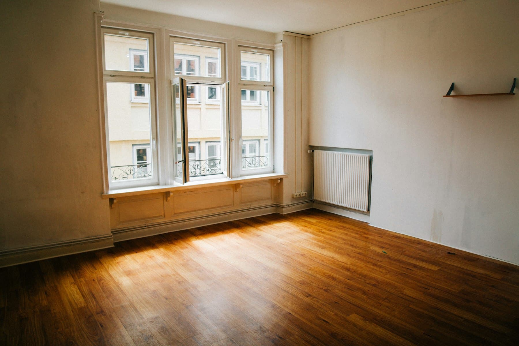 Habitación vacía con suelo de madera y ventanal antes de la reforma