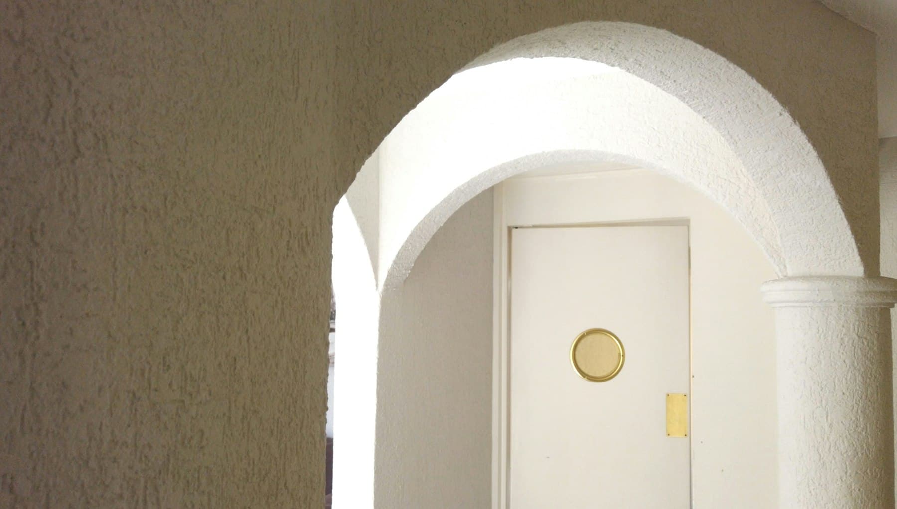 Arco de yeso encalado que enmarca una puerta blanca con tirador de latón