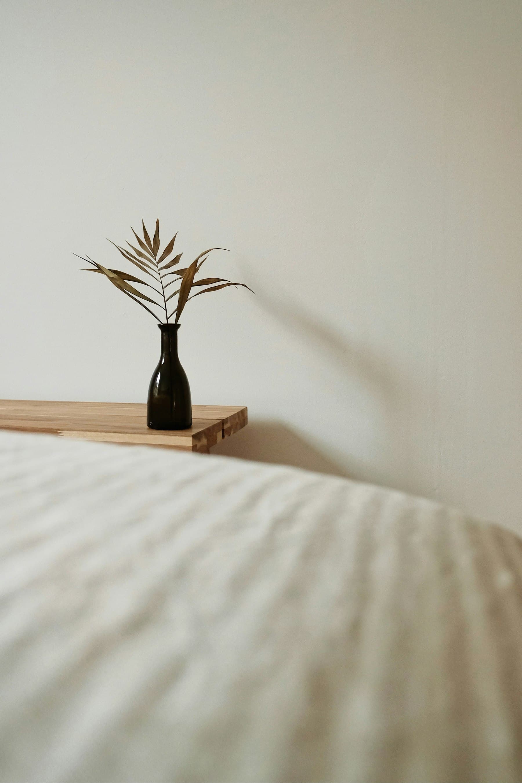 Jarrón negro con una hoja seca sobre una balda de madera, visto desde la cama